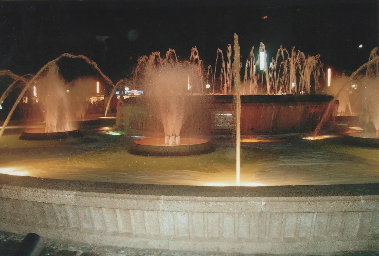 A round fountain in Salou with several jets of water lit orange against a dark night sky